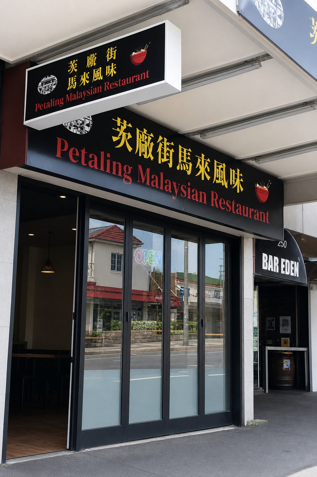 A black fascia sign reading 茨廠街馬來風味 in yellow above Petaling Malaysian Restaurant in red, over folding glass doors with an OPEN neon in the window