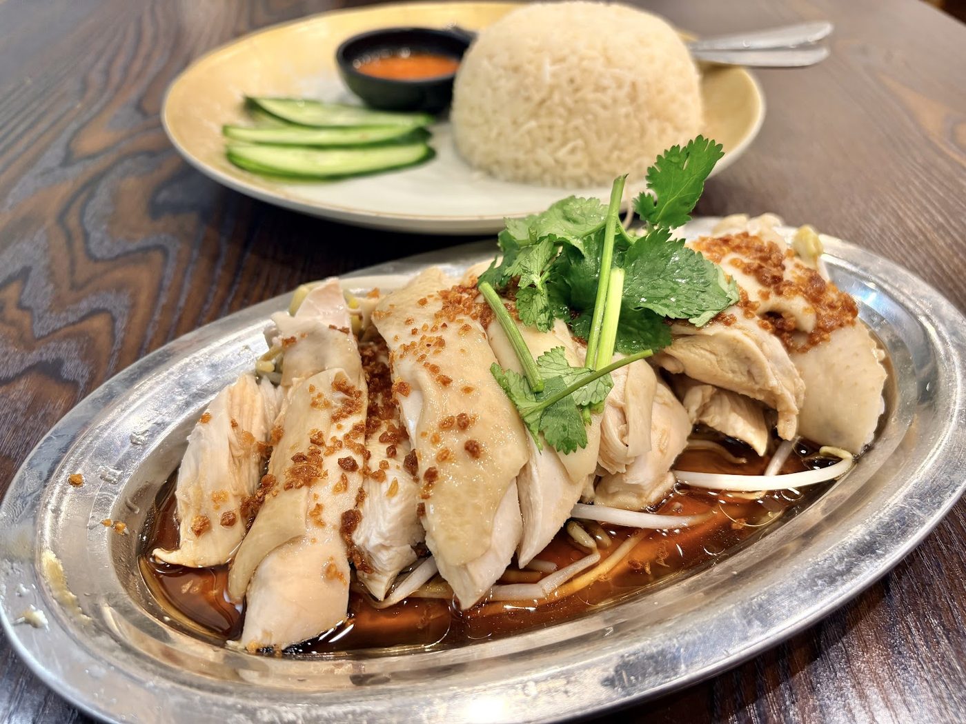 Poached chicken sliced over bean sprouts in a pool of dark soy on a silver oval platter, fried garlic and coriander scattered on top